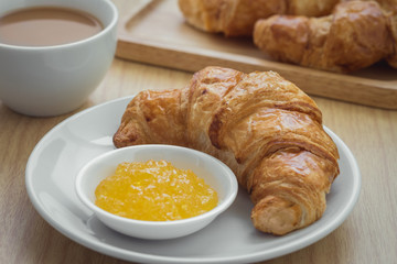 Croissant with jam on plate and coffee cup