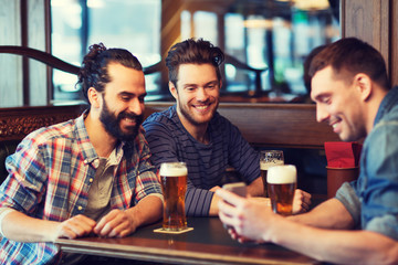 male friends with smartphone drinking beer at bar