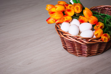 Easter eggs and tulips in basket on wooden table