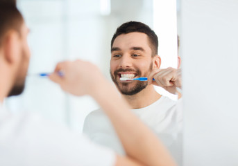 man with toothbrush cleaning teeth at bathroom