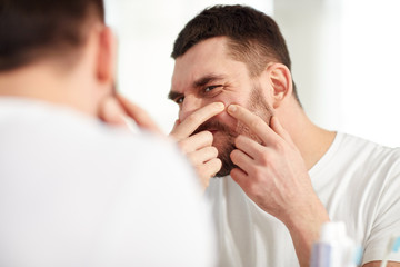 man squeezing pimple at bathroom mirror