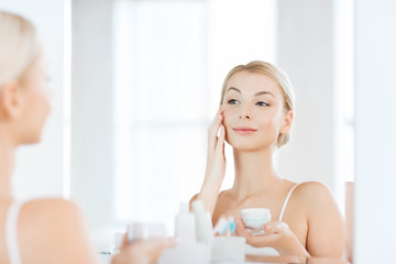 Obraz na płótnie Canvas happy woman applying cream to face at bathroom