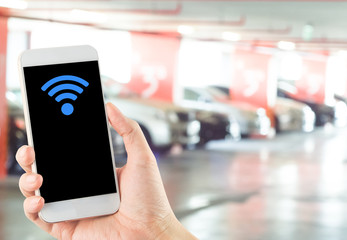 smartphone in hand with wi-fi icon on blurred car parking area