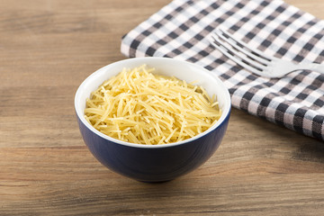Blue bowl with uncooked noodles and fork on wooden table
