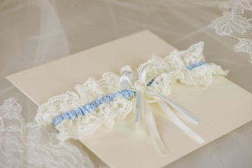 Creamy wedding invitation with a blue and white wedding garter resting on ebroidered lace