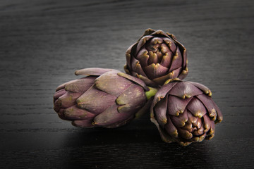Obraz premium Tre carciofi freschi appoggiati sul tavolo di legno 