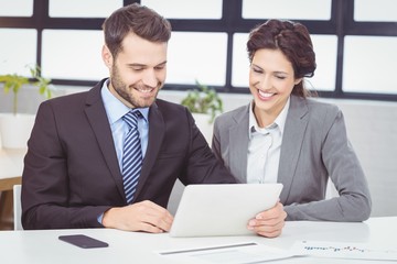 Happy business people discussing over digital tablet at desk in office