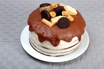 Cake, glazed with milk chocolate and decorated with waffles and cookies, on white plate
