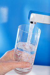 Filling up a glass of water . Blue background.