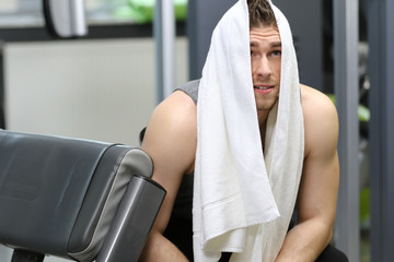 Young handsome muscled man with a towel on head at the gym