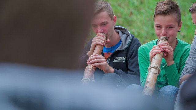 Boys playing the didgeridoo near the camp fire 
