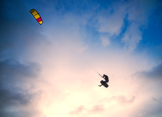 Kiteboarder performing a jump against sky at sunset