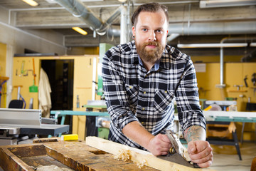 Smiling carpenter work with plane on wood plank in workshop