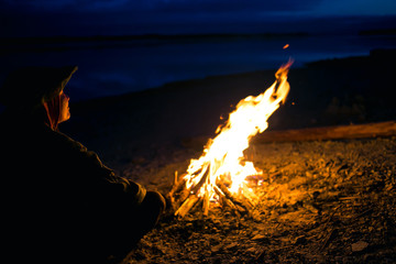 the silhouette of girl tourist around the campfire at night on the river shore