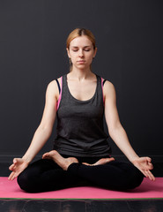 Fototapeta premium Young woman is sitting in the lotus pose with closed eyes
