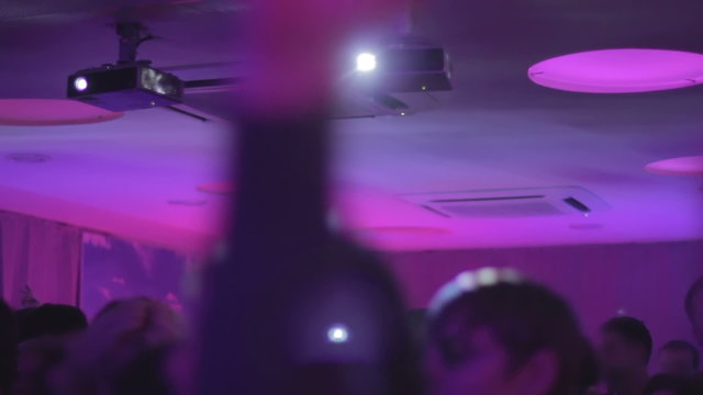 Happy crowd enjoying nightlife in club, waving hands to music on the dance floor
