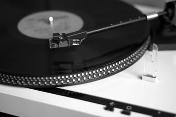 Turntable in silver case playing a vinyl record with red label. Black and white photo side view closeup