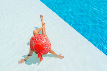 Woman sitting in a swimming pool in a sunhat