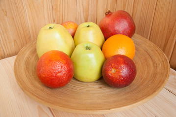 Naklejka na ściany i meble Apples, oranges and pomegranate on a round wooden plate