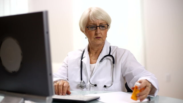 Senior woman doctor looks at pills and writes