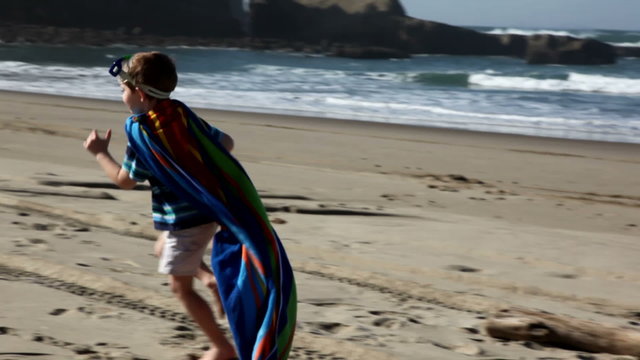 Young boy running on beach with towel