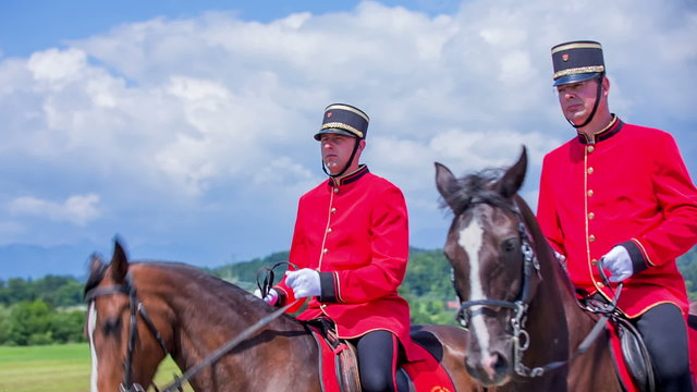 Two men in red uniforms are riding horses