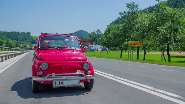 An old couple talking in a red vintage car