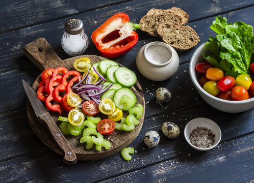 Ingredients to prepare vegetable salad - tomatoes, cucumber, celery, bell pepper, red onion, quail eggs, garden herbs and spices on a rustic wooden board. Healthy food