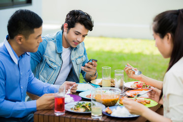 Asian man sitting on a smartphone during the meal. Group with fr