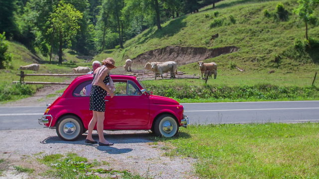 An older couple is going into their small vintage red car