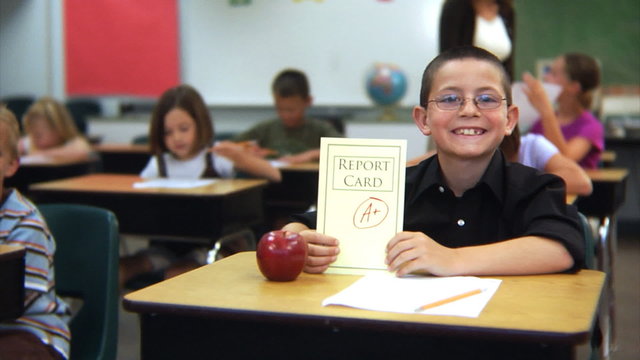 Child sitting at school desk with A+ report card