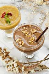 Chocolate malt frappe and passion fruit mixed drinks on marble table with dried flowers