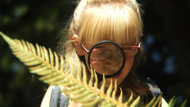 Young girl looks at fern with magnifying glass