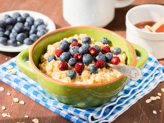 Oatmeal porridge in a green bowl with blueberries and wild strawberries on checkered napkin