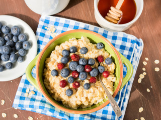 Oatmeal porridge in a green bowl with blueberries and wild strawberries on checkered napkin