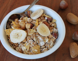 Müsli mit Nüssen, Mandeln und Banane auf einem braunen Holztisch