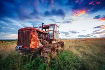 ld rusty tractor in a field on sunset