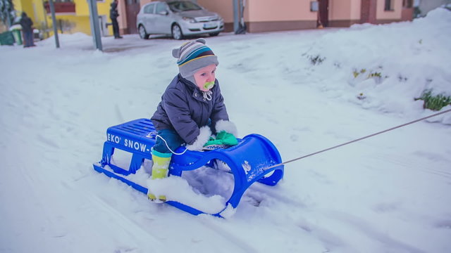 A boy is pulling a small boy on a sled across the street