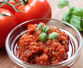 rotes Pesto mit Basilikum garniert und Zutanten im Hintergrund auf einem braunen Holztisch