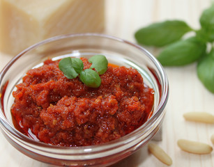 rotes Pesto mit Basilikum garniert und Zutanten im Hintergrund auf einem Holztisch