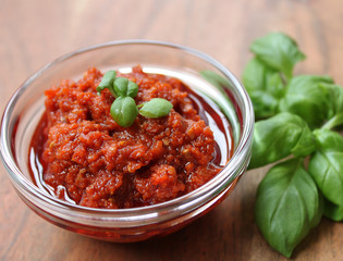 rotes Pesto mit Basilikum garniert auf einem braunen Holztisch