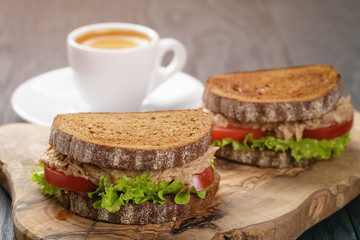 rye bread sandwich with tuna and coffee on wood background
