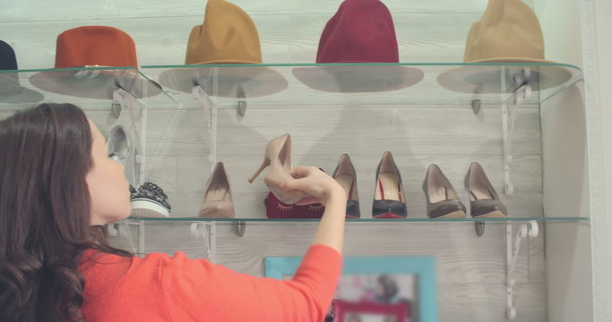 Young brunette looking at shoes on shelf in fashion store and choosing beige patent high heels