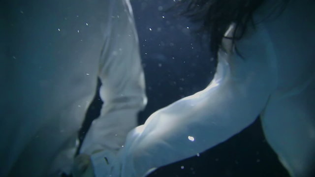 A young couple is holding hands and swimming under water