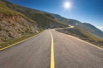 Driving on an empty mountain road towards the sun