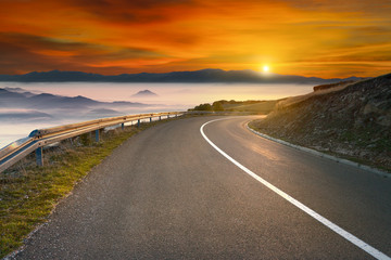 Driving on asphalt mountain road towards the sun