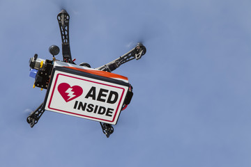 UAV drone quadrocopter with modern GPS navigation transporting Automated external defibrillator AED, against blue sky, space for text - obrazy, fototapety, plakaty