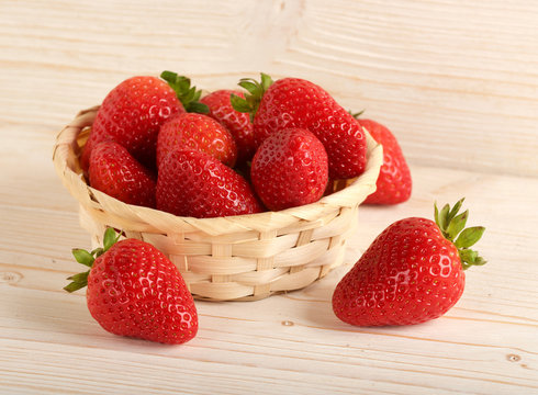 strawberries in small basket on a wooden background