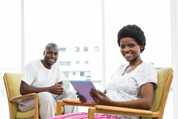 Obraz premium Smiling pregnant woman using tablet and man sitting