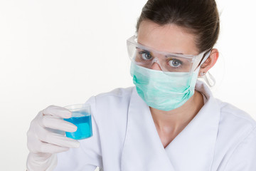 Brunette female scientist in protective goggles holds blue liquid tube